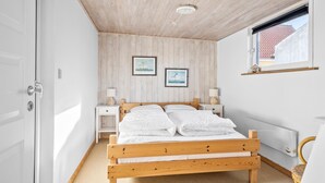 A bedroom with a wooden bed, two bedside tables with lamps, a radiator, and two framed pictures on the wall. - Cozy home in Thyborøn with sauna (Thyborøn)
