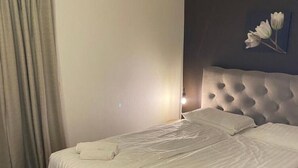 A neatly made bed with white linens and rolled towels, a tufted headboard, and a wall-mounted flower decoration.