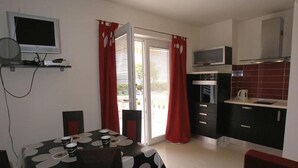 A compact kitchen with a dining area, featuring a table with a black and white patterned tablecloth, red curtains, and a TV mounted on the wall.