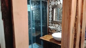 Un baño con cabina de ducha de vidrio, tocador de madera con lavabo y pared decorada con leña apilada.