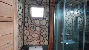 Un baño con pared de piedra, una ventana pequeña y una cabina de ducha de vidrio.
