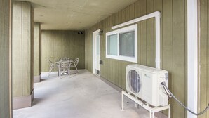 A corridor with a window, a white air conditioning unit, and a metal table with chairs.