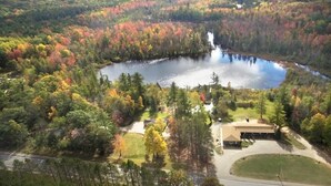 A lake surrounded by autumn-colored trees, a building with a paved driveway, and a road in the foreground.