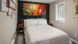 A bedroom with a bed, a window with blinds, and a large abstract painting on the wall.