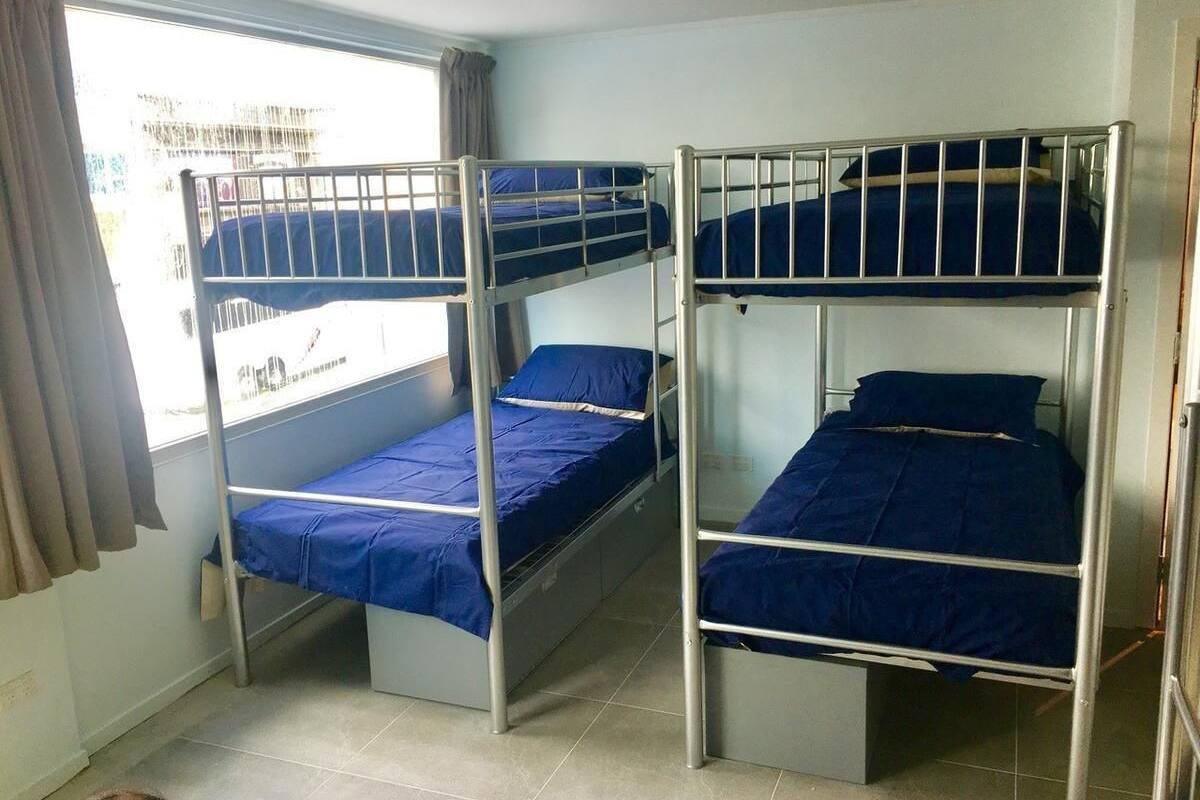 Quarto com três beliches, cada um com colchão azul e estrutura de metal.