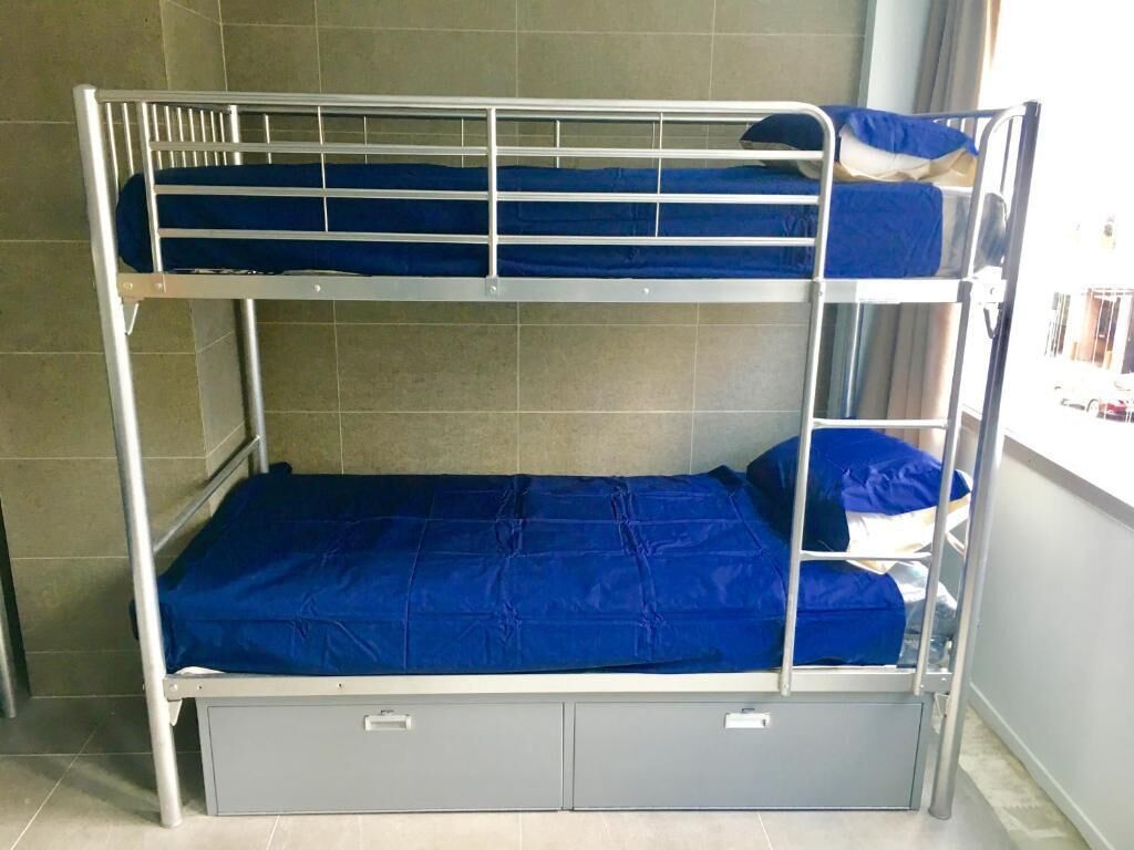A bunk bed with two levels, each with a blue mattress and metal frame.