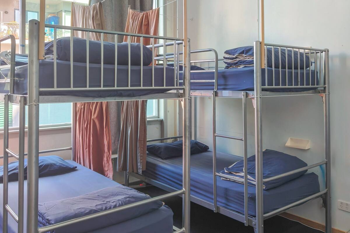 Um quarto de dormitório com beliches, janela com cortinas e vista para o edifício exterior.