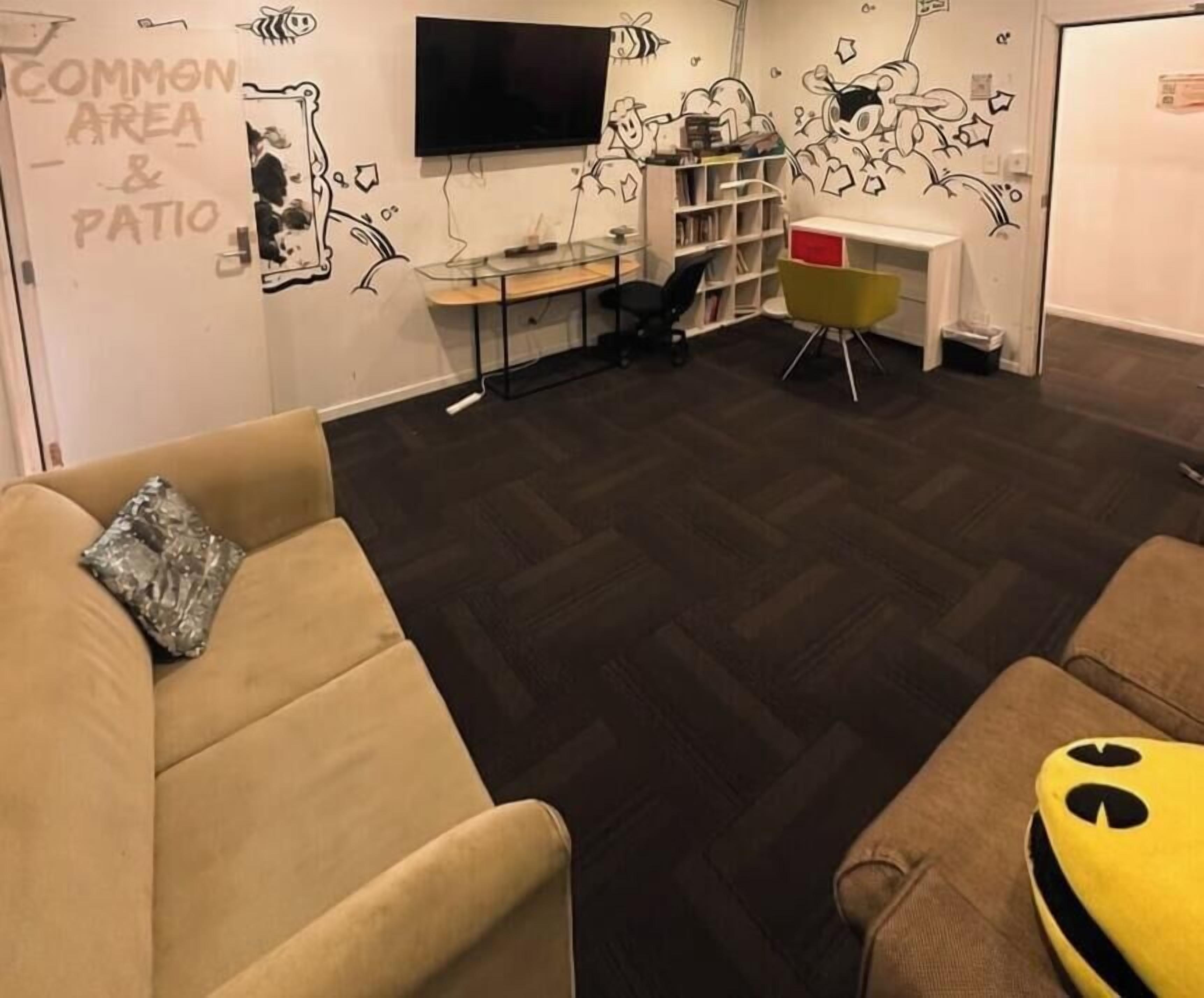 Una habitación con sofá, escritorio, televisor y estantería.
