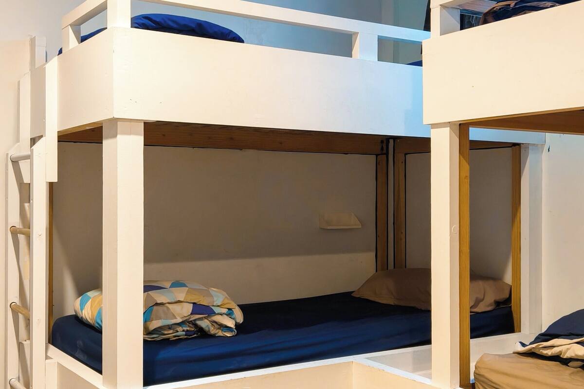 Quarto com beliche, escada no lado esquerdo, prateleira pequena e tomada na parede direita.
