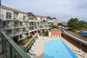 Un hotel de varios pisos con piscina, balcones y vista a la calle.