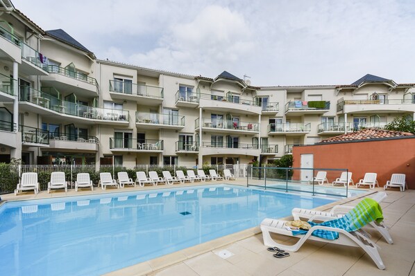 Una piscina con sillas de descanso y un edificio con varios balcones.