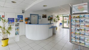 Aula, jossa on valkoinen vastaanottotiski, karttanäyttö ja seinillä informatiivisia julisteita.