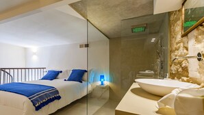 Una habitación de hotel moderna con cama, mesita de noche, lámpara y un baño con lavabo y ducha.
