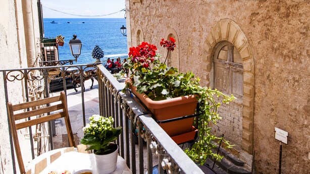 Un balcón con una mesa para dos, plantas en macetas y vista al mar.