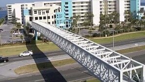 A modern building with multiple floors and balconies, a pedestrian bridge, and a parking area. - Welcome to Relaxation! Gulfside Villa 408 (Fort Walton Beach)