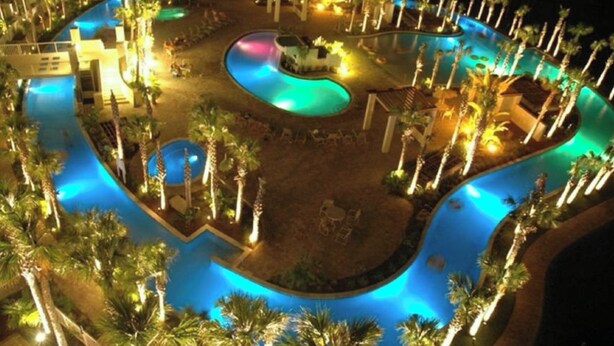An aerial view of a resort with multiple swimming pools, palm trees, and illuminated areas. - Welcome to Relaxation! Gulfside Villa 408 (Fort Walton Beach)