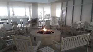 A circular fire pit surrounded by white Adirondack chairs in a covered outdoor area with a view of the sky and trees. - Seawatch 2BR/2BA South Tower Ocean View Condo - Fantastic Resort Myrtle Beach SC (Myrtle Beach)