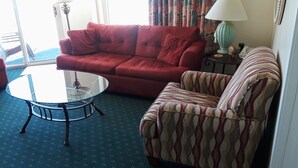 A living room with a red sofa, a patterned armchair, and a glass coffee table. - Seawatch 2BR/2BA South Tower Ocean View Condo - Fantastic Resort Myrtle Beach SC (Myrtle Beach)
