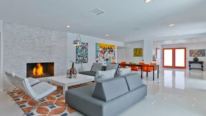 Een moderne woonkamer met een open haard, een bank, een eethoek met oranje stoelen en een keuken op de achtergrond.