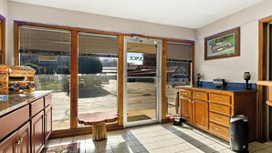 A kitchen with a sliding glass door leading to a patio, wooden cabinets, a small table, and a trash can. - Knights Inn Collinsville Va (Collinsville)