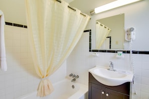 A bathroom with a bathtub, a sink, a hairdryer, and a mirror.