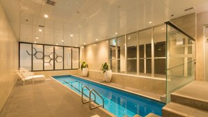 Una piscina interior con paredes de vidrio transparente, bancos y plantas en macetas.