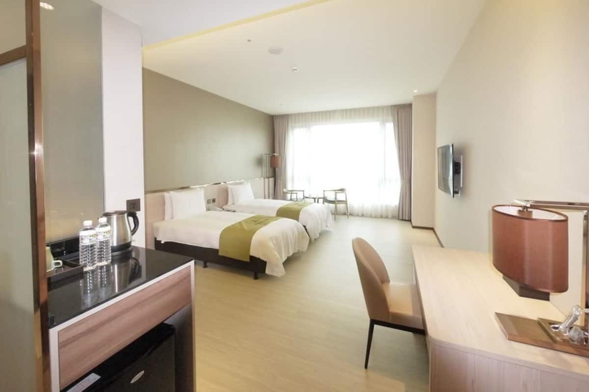 Una habitació d'hotel amb llit, escriptori, cadira, televisió i finestra amb cortines.