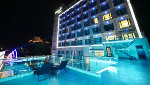 Ein mehrstöckiges Hotel mit Poolbereich auf dem Dach, ausgestattet mit Glasgeländern und Liegestühlen.