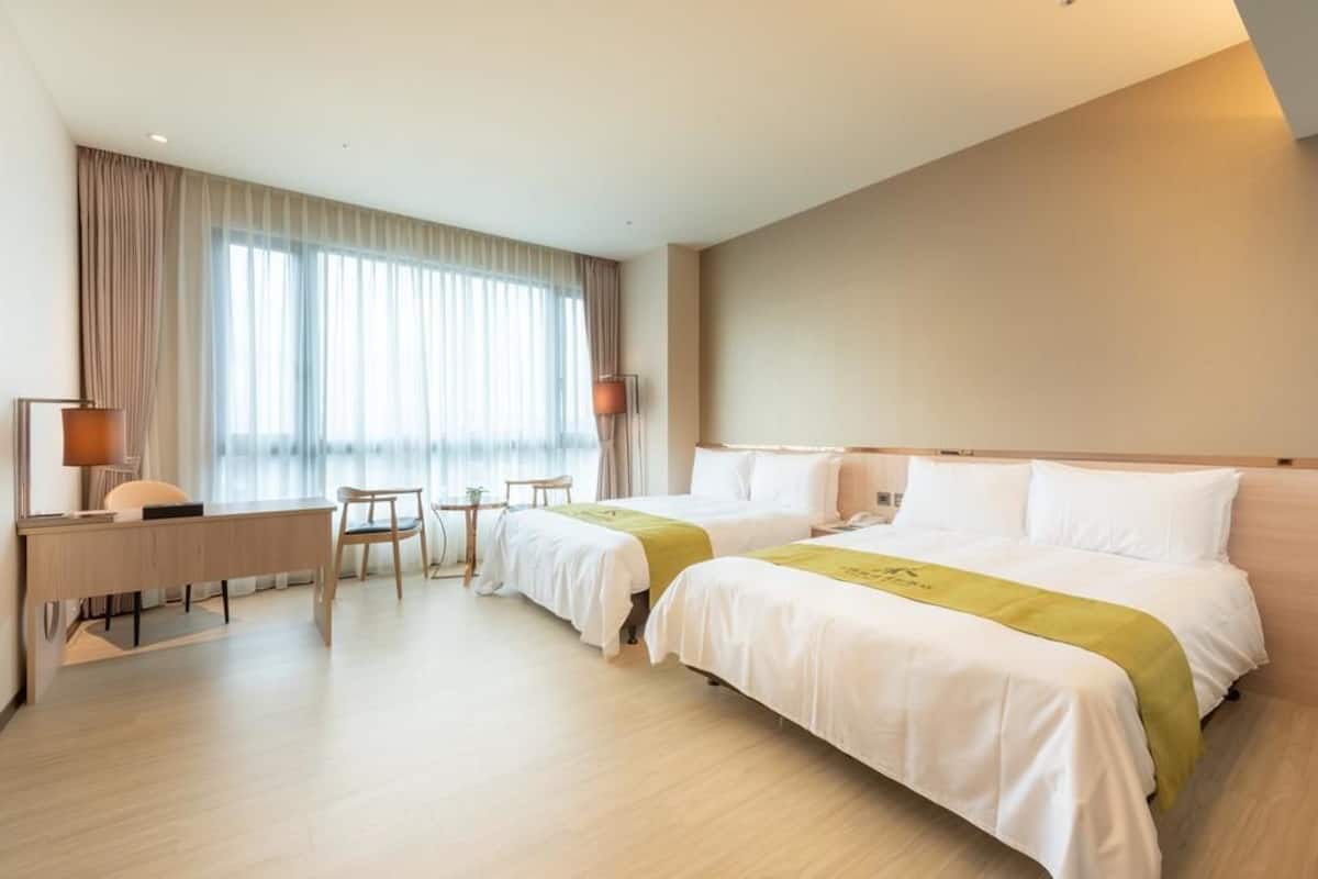 Habitació d'hotel amb dos llits, una taula de treball, una cadira i una taula petita.
