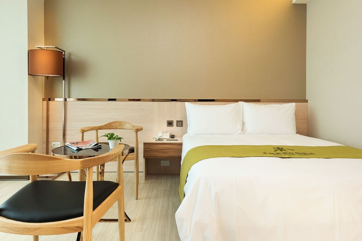 Habitació d'hotel amb llit, escriptori, cadira, làmpada i tauleta de nit.