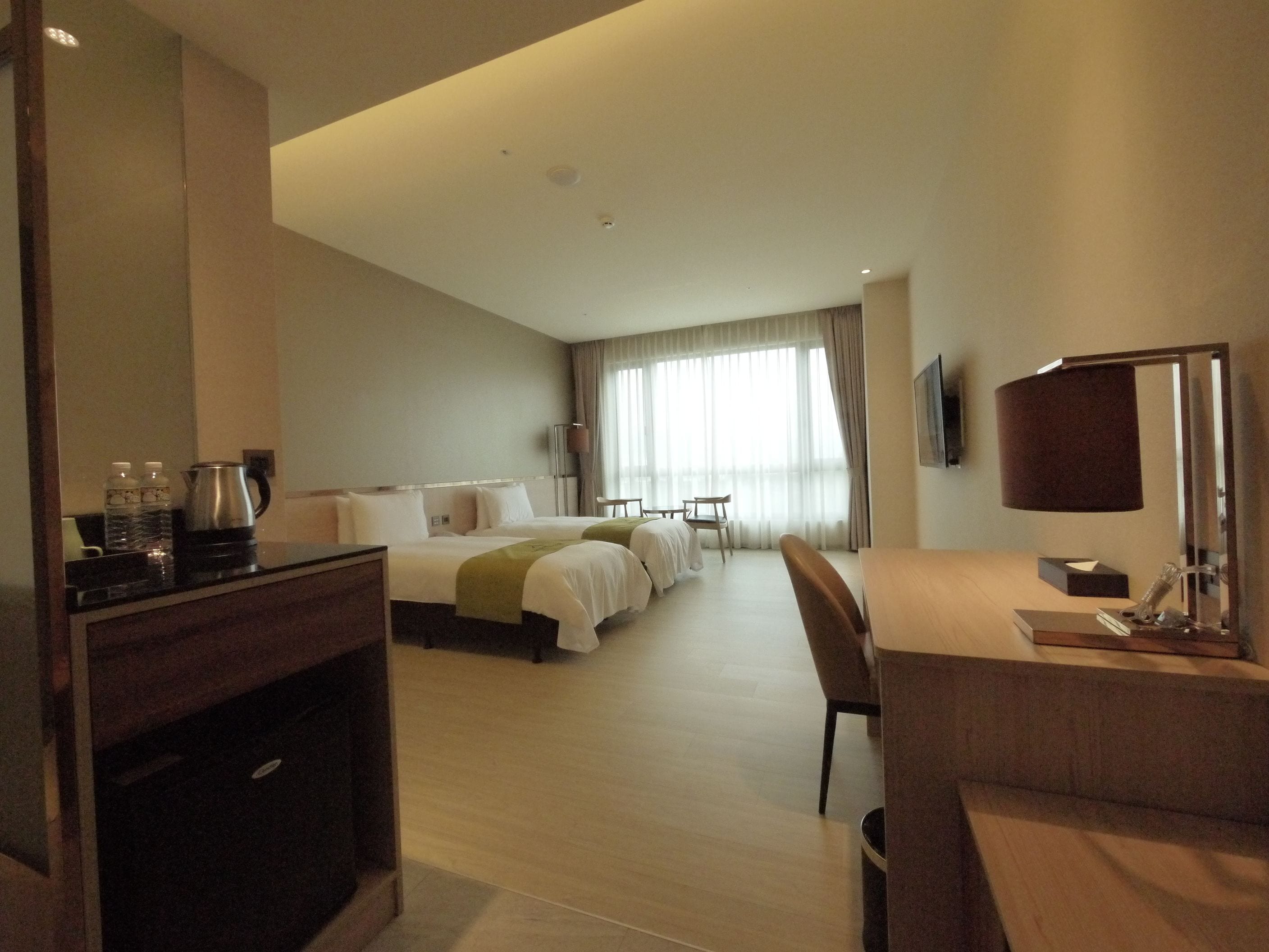 A hotel room with a bed, a desk, a chair, a TV, and a window with curtains.