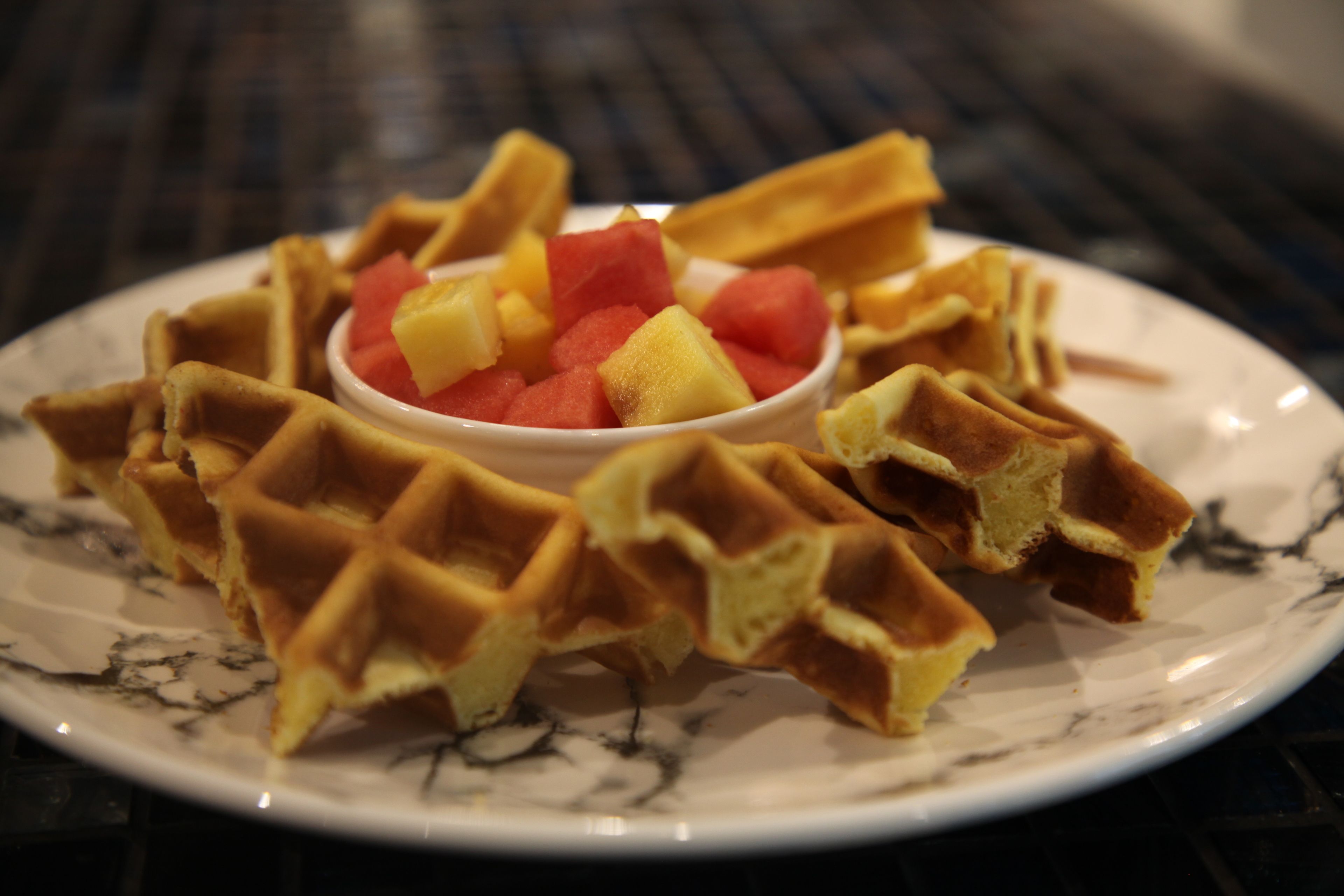 A plate of waffles with a bowl of diced fruit in the center.