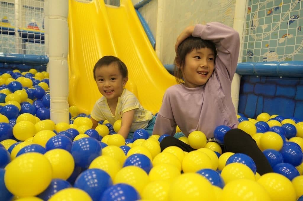Kinderen spelen in een bollenbak met een gele glijbaan.