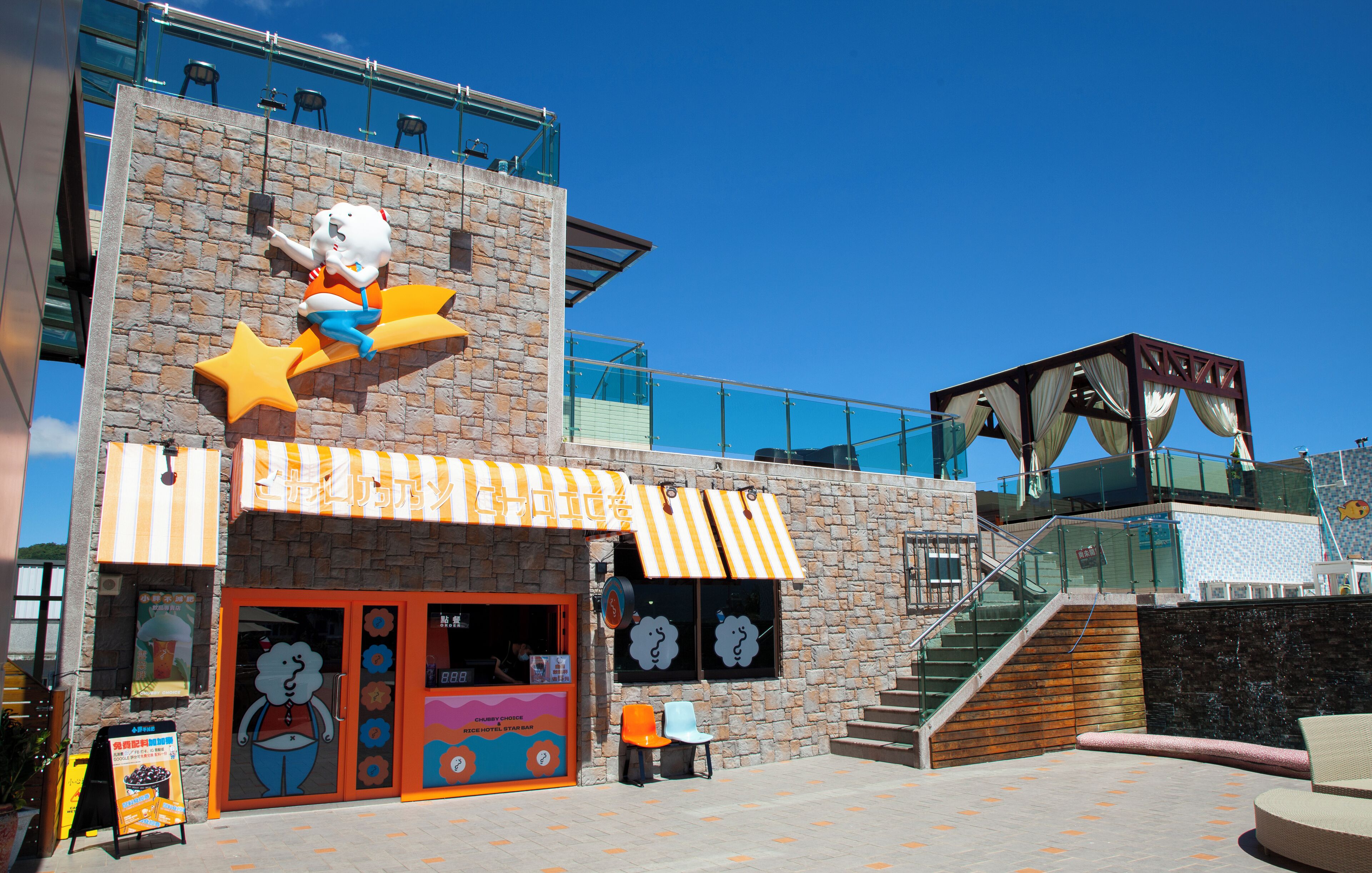 A building with a cartoon character on the facade, a staircase, and a covered area with a view of the sky.