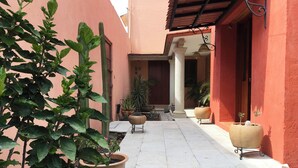 A courtyard with potted plants, a tiled floor, and a red building facade. - La Casita del Abuelo, beautiful Oaxaca typical house  (San Felipe del Agua)