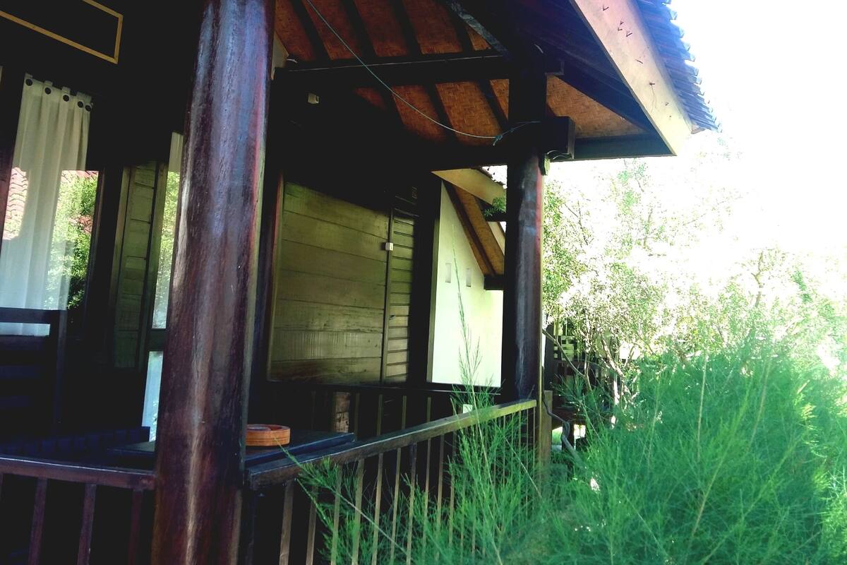 A wooden structure with a sloped roof, a wooden railing, and a view of greenery.