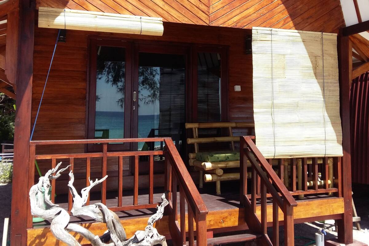 A wooden cabin with a porch, a staircase, and a large window.
