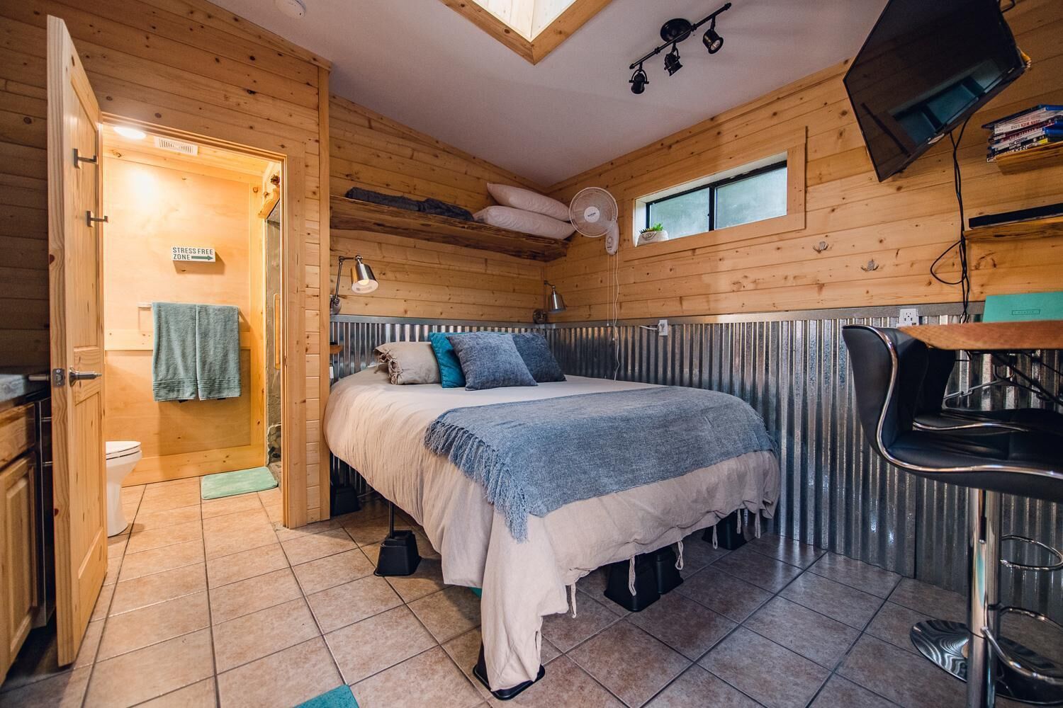 A cozy cabin-style room with a bed, a small kitchenette, a fan, and a window.