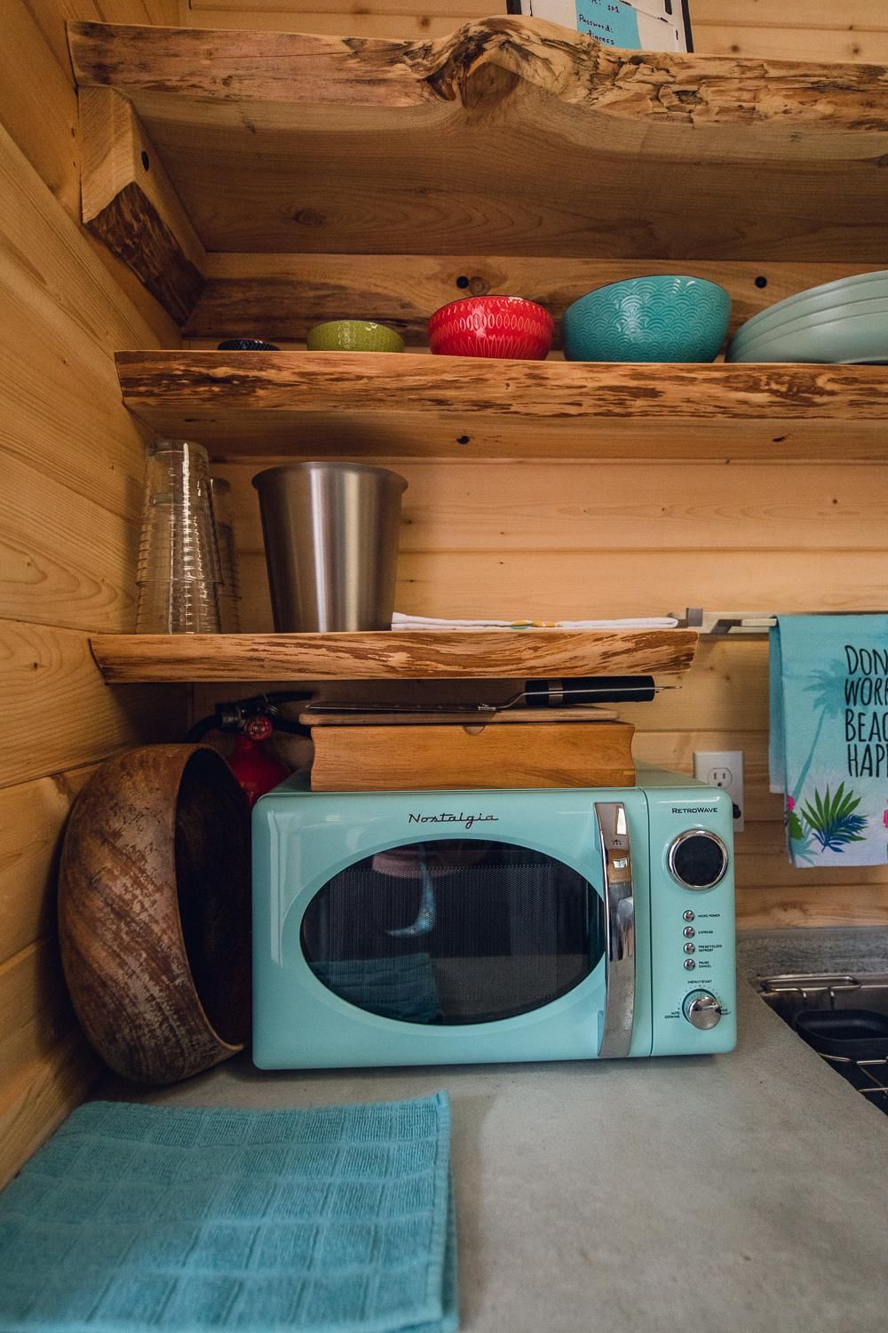 A kitchen with a vintage-style microwave, wooden shelves, and a sign that reads "DON'T WORRY BECAUSE HAPPINESS IS ON THE WAY."