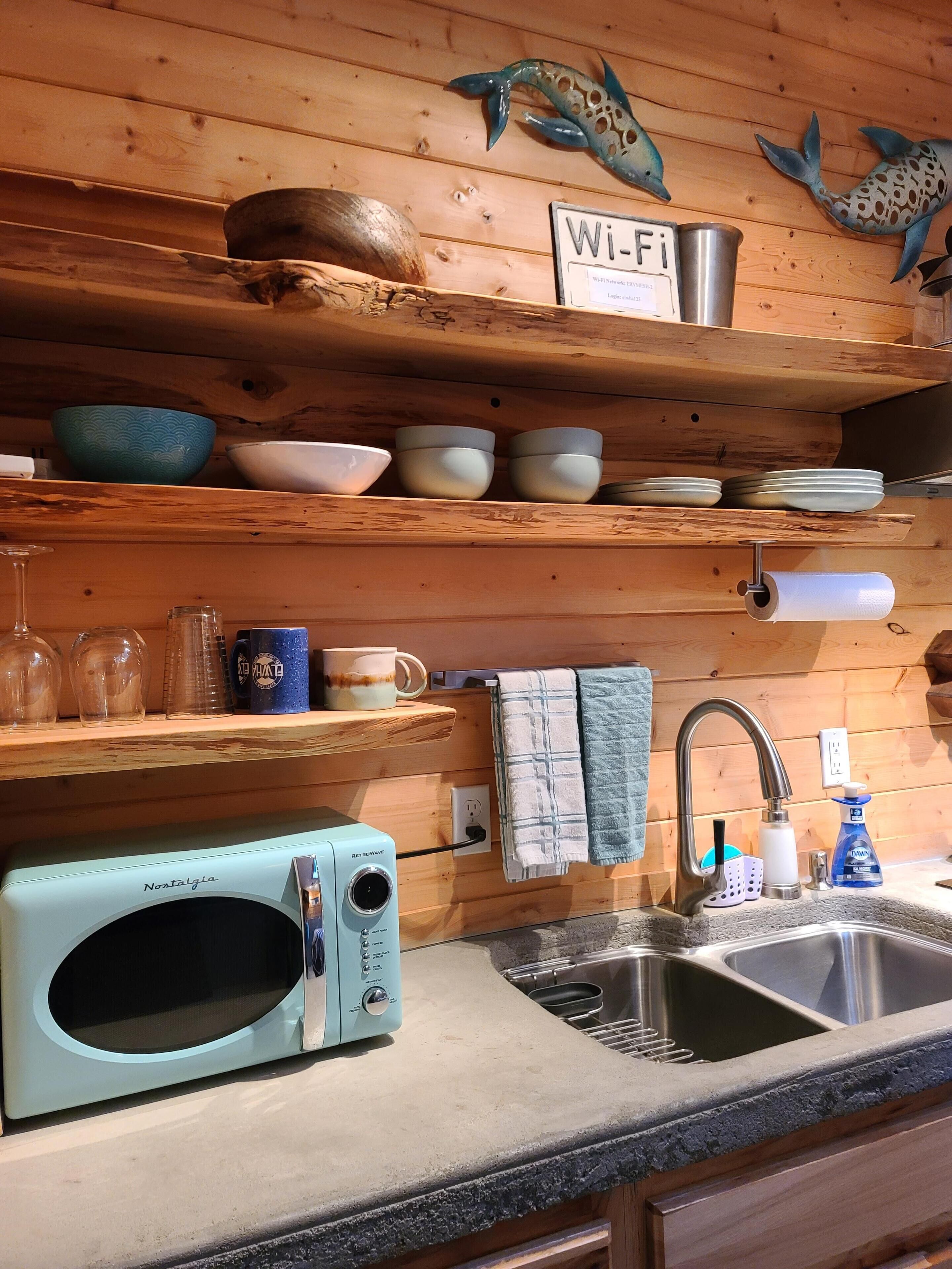 Une cuisine avec des étagères en bois où sont posés des bols, un four à micro-ondes et un panneau indiquant la présence d’une connexion Wi-Fi.