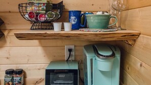 Innenansicht einer Holzhütte mit einem Regal, das eine Kräutertee-Auswahl, Tassen und eine Kaffeemaschine beherbergt.