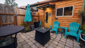 Ein Holzhaus mit einer Terrasse, komplett mit Tisch, Stühlen und einer kleinen Feuerstelle.