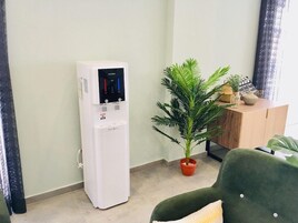 A water dispenser, a potted plant, and a wooden cabinet in a room with light-colored walls and a tiled floor.