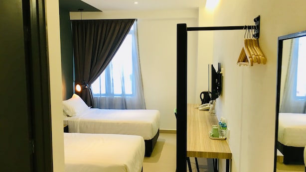 Une chambre d’hôtel avec deux lits, un bureau avec un téléphone et une bouteille d’eau, et un miroir au mur.