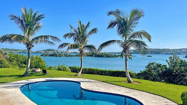 A swimming pool with a curved edge, surrounded by a well-maintained lawn and palm trees. -  Romantic - Pool & Ocean View, WiFi, Kayaks, parking  (Hamilton)