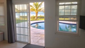 A room with a sliding glass door leading to a pool area, a window with blinds, and a small mat at the door entrance. -  Romantic - Pool & Ocean View, WiFi, Kayaks, parking  (Hamilton)