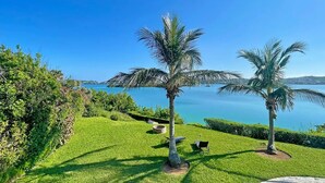 A well-maintained lawn with two palm trees and a bench, overlooking a calm body of water with distant landforms. -  Romantic - Pool & Ocean View, WiFi, Kayaks, parking  (Hamilton)