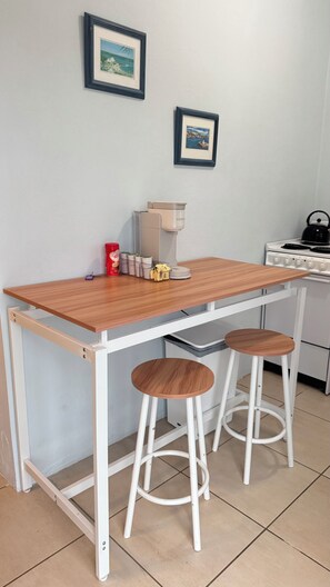 Een kleine kitchenette met een houten tafel, twee krukjes, een koffiezetapparaat en een fornuis.