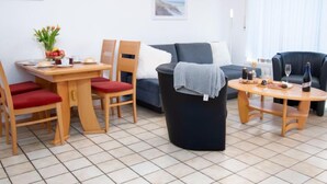 Ein möbliertes Wohnzimmer mit Esstisch, Stühlen, einer Couch, einem Couchtisch und einem Mülleimer.
