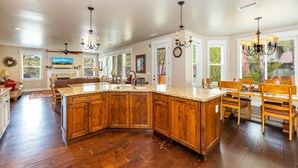 Una cocina amplia con armarios de madera, encimeras de granito y una isla grande. Varias ventanas ofrecen luz natural y vistas al exterior.